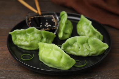 Delicious green dumplings (gyozas) and soy sauce on wooden table, closeup