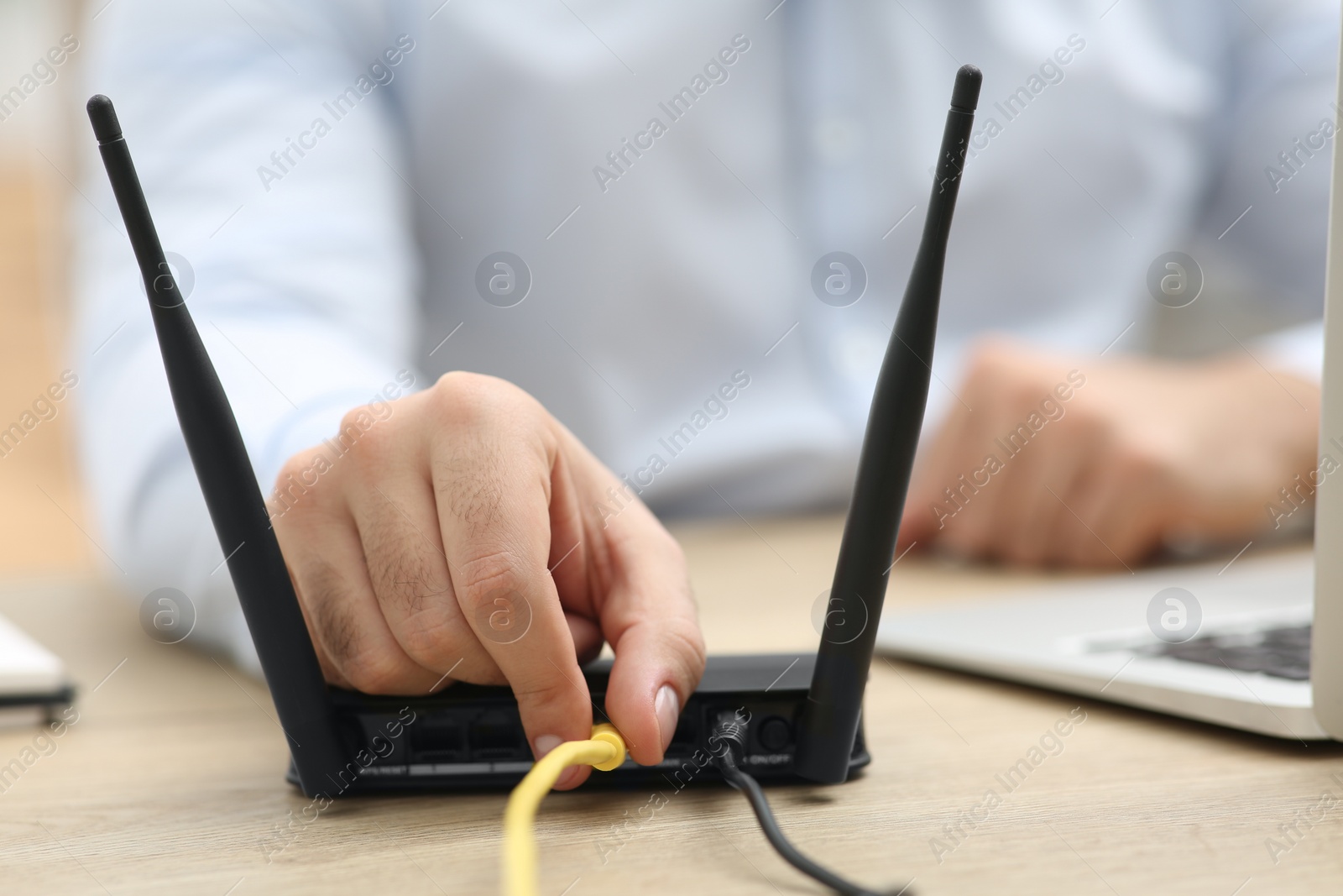 Photo of Man inserting cable into Wi-Fi router at wooden table indoors, closeup