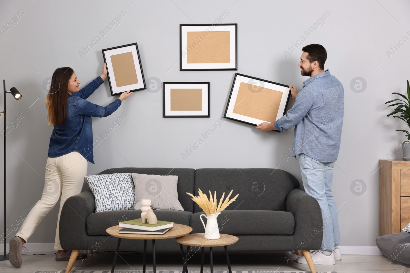 Photo of Man and woman hanging picture frames on gray wall at home