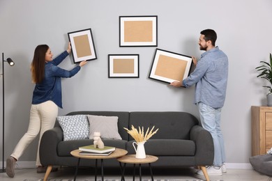 Photo of Man and woman hanging picture frames on gray wall at home