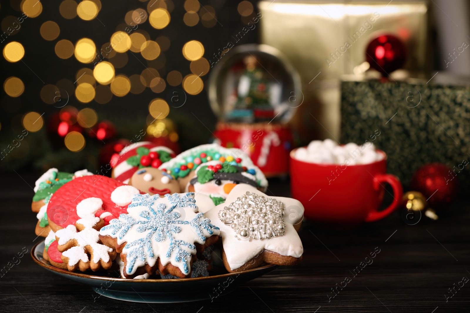 Photo of Sweet Christmas cookies and decor on black wooden table against blurred festive lights