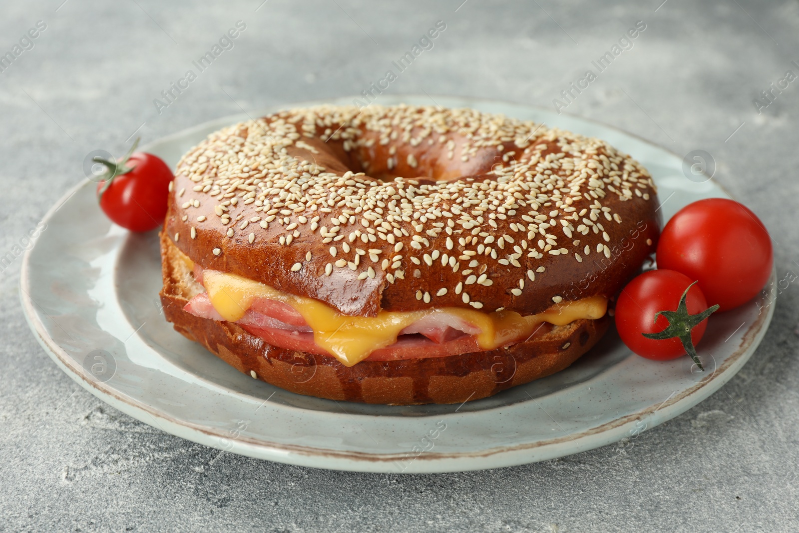 Photo of Delicious bagel with ham, cheese and tomatoes on light grey textured table