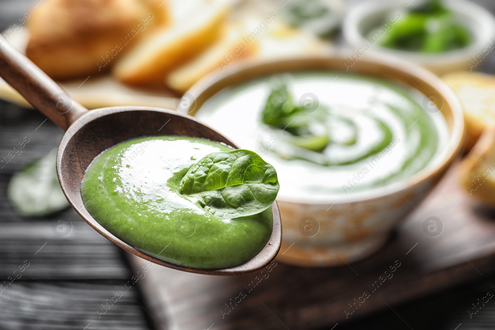 Photo of Spoon with fresh vegetable detox soup made of spinach on blurred background, closeup