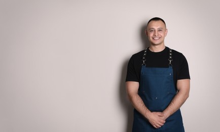 Photo of Portrait of happy young waiter in uniform on light background