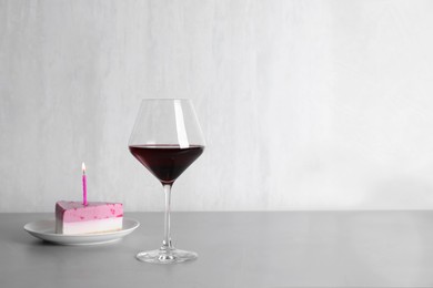 Glass with red wine and piece of delicious cake on table against white background, space for text