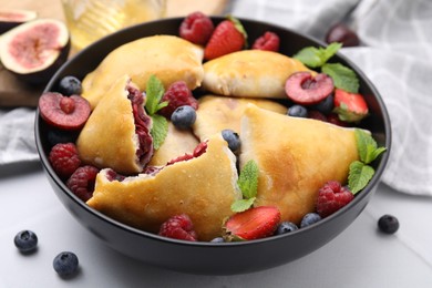 Photo of Bowl with delicious samosas, berries and mint leaves on white tiled table, closeup