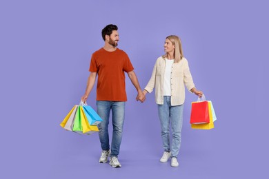 Family shopping. Happy couple with many colorful bags on violet background