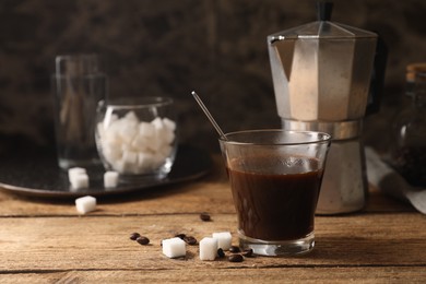 Photo of Brewed coffee in glass, moka pot, beans and sugar cubes on wooden table, space for text
