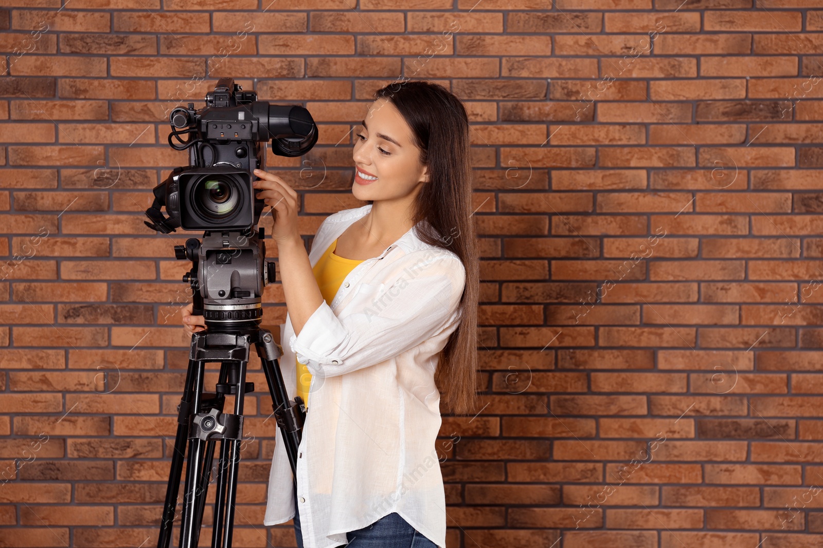 Photo of Operator with professional video camera near brick wall, space for text