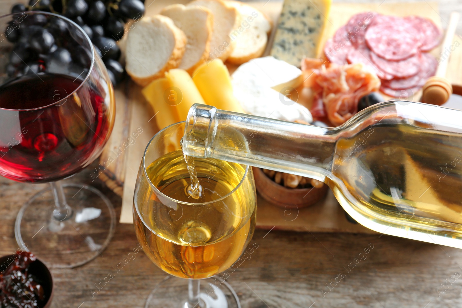 Photo of Pouring white wine into glass on table with delicious food