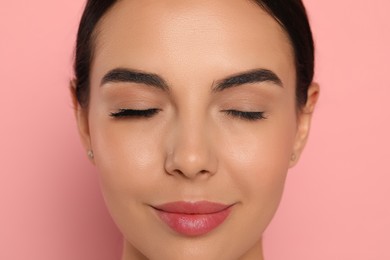 Beautiful young woman showing extended and ordinary eyelashes on pink background, closeup