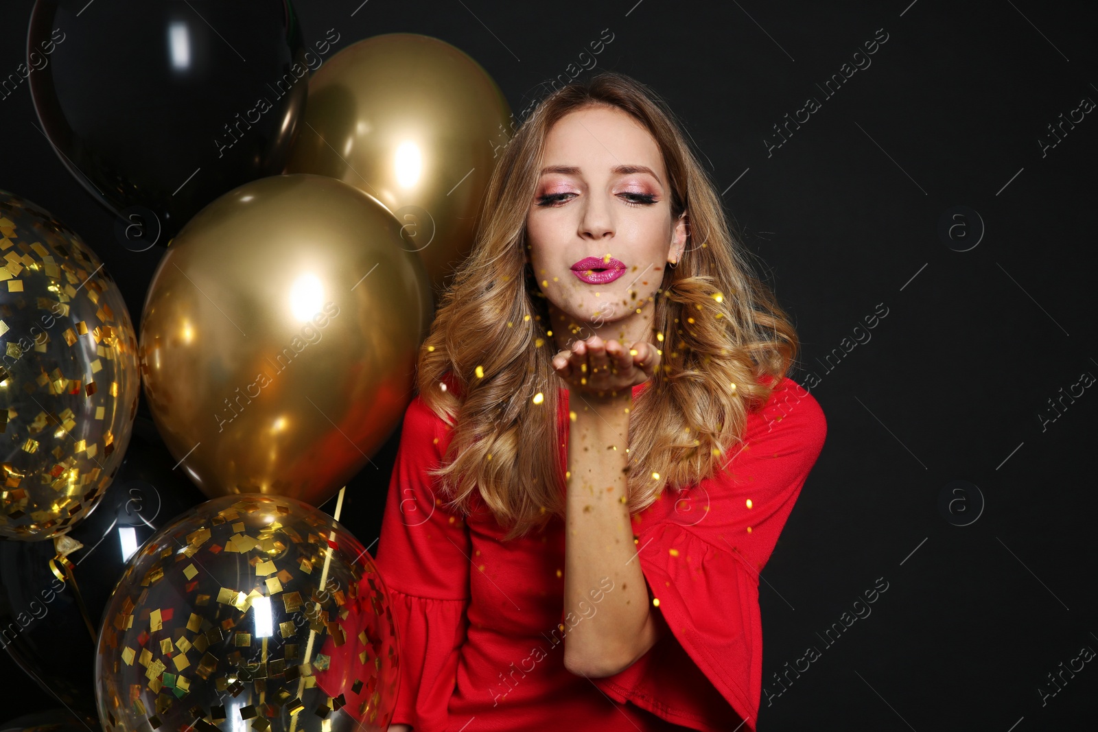 Photo of Happy woman with air balloons blowing glitter on black background. Christmas party