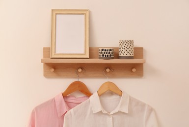 Photo of Wooden shelf with fashionable clothes, candles and photo frame on beige wall. Interior element