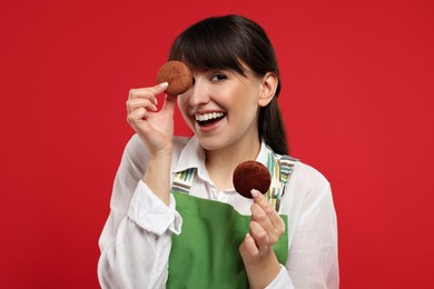 Photo of Happy professional confectioner in apron holding delicious macarons on red background