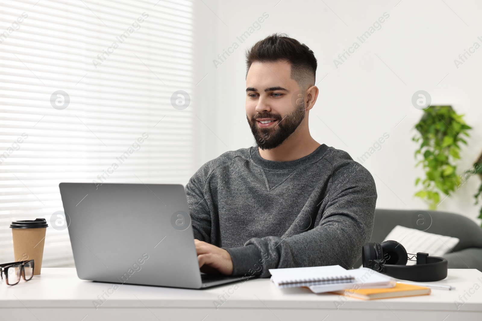 Photo of E-learning. Young man using laptop during online lesson at white table indoors