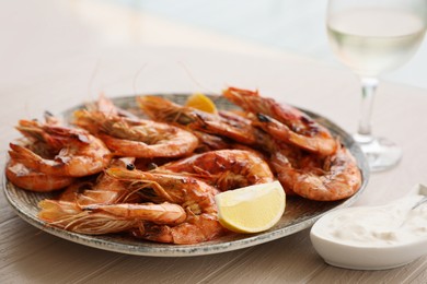 Photo of Plate of delicious cooked shrimps served with lemon, sauce and wine at table, closeup