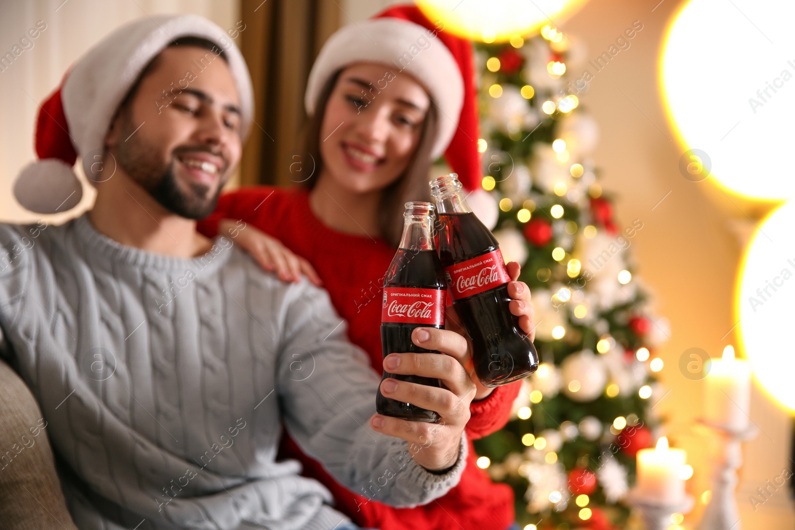 Photo of MYKOLAIV, UKRAINE - JANUARY 27, 2021: Young couple holding bottles of Coca-Cola at home, focus on hands. Christmas atmosphere