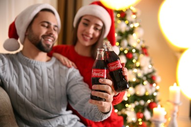 Photo of MYKOLAIV, UKRAINE - JANUARY 27, 2021: Young couple holding bottles of Coca-Cola at home, focus on hands. Christmas atmosphere