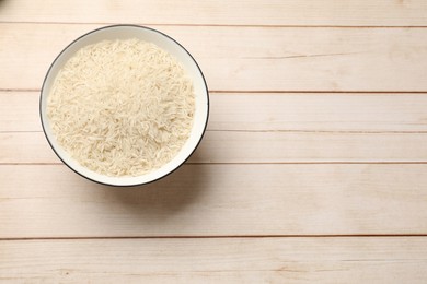 Photo of Raw basmati rice in bowl on white wooden table, top view. Space for text