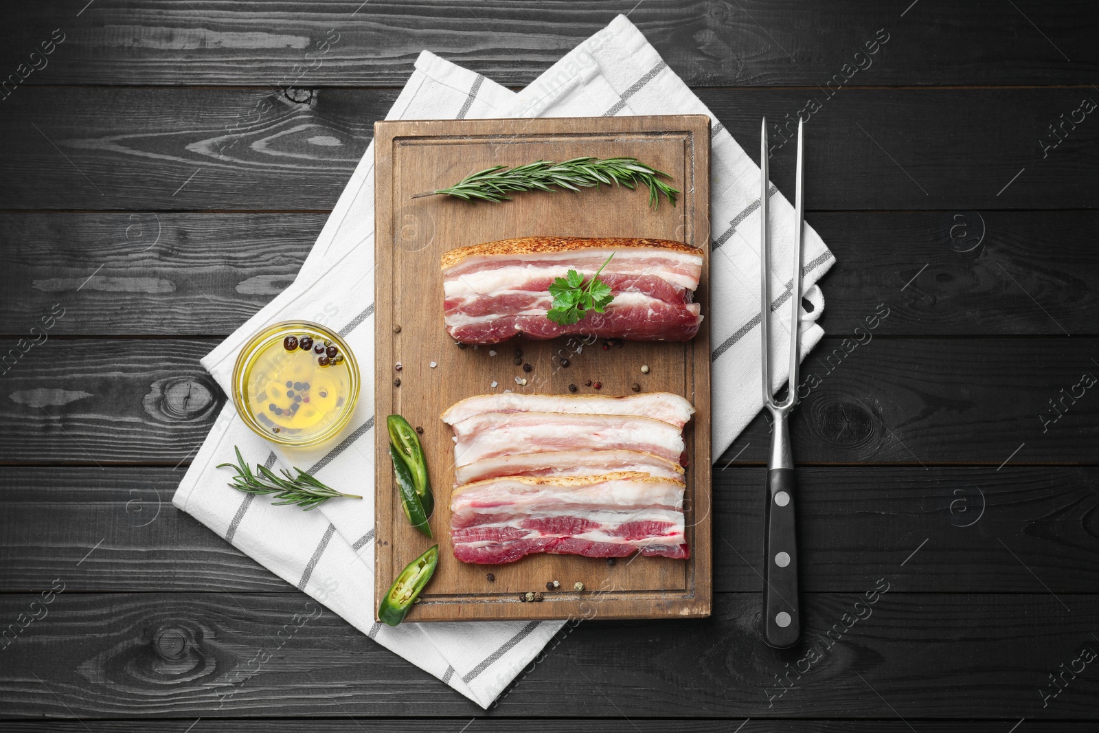 Photo of Pieces of raw pork belly, chili pepper, peppercorns, rosemary and parsley on black wooden table, flat lay