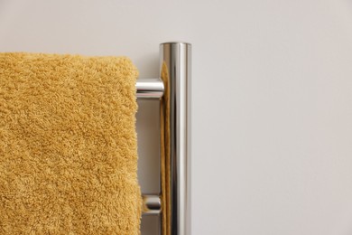 Photo of Heated rail with yellow towel on white wall, closeup. Space for text