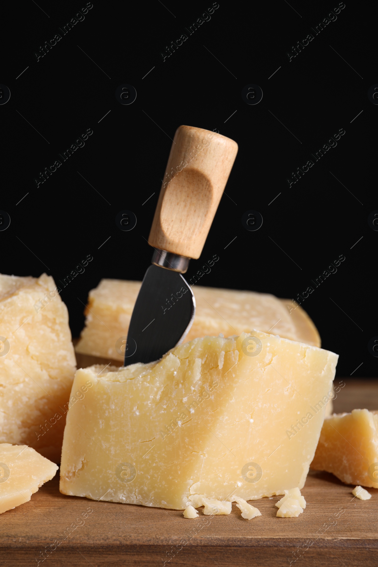 Photo of Parmesan cheese with knife on wooden board, closeup