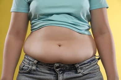 Photo of Woman with excessive belly fat on yellow background, closeup. Overweight problem
