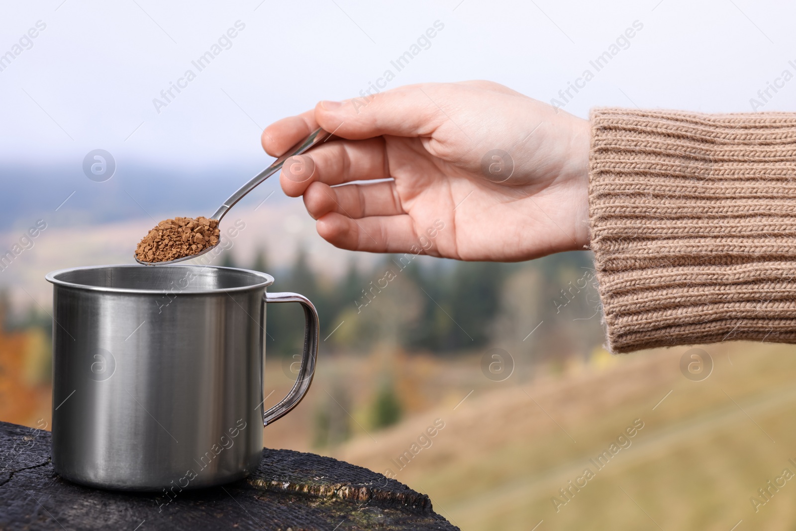 Photo of Woman pouring instant coffee into mug in mountains, closeup