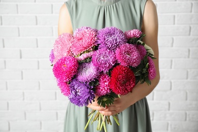 Woman holding bouquet of beautiful aster flowers against white brick wall, closeup