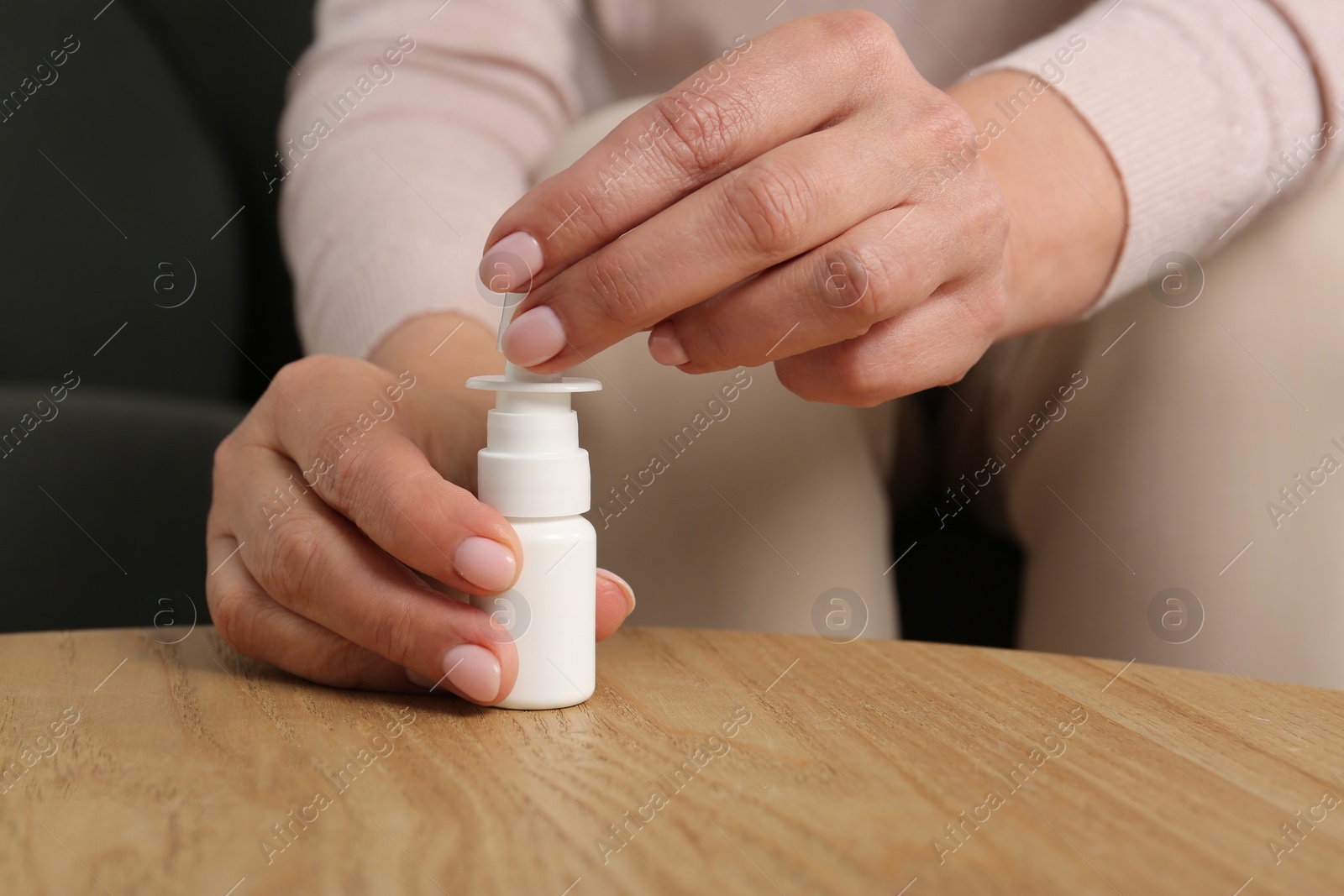 Photo of Woman opening nasal spray at wooden table indoors, closeup