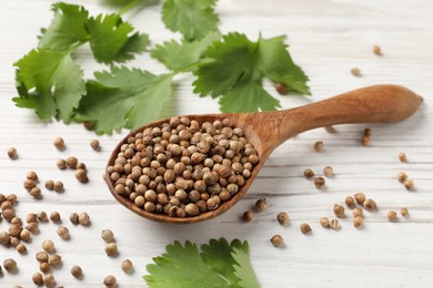 Photo of Spoon with dried coriander seeds and green leaves on wooden table, closeup