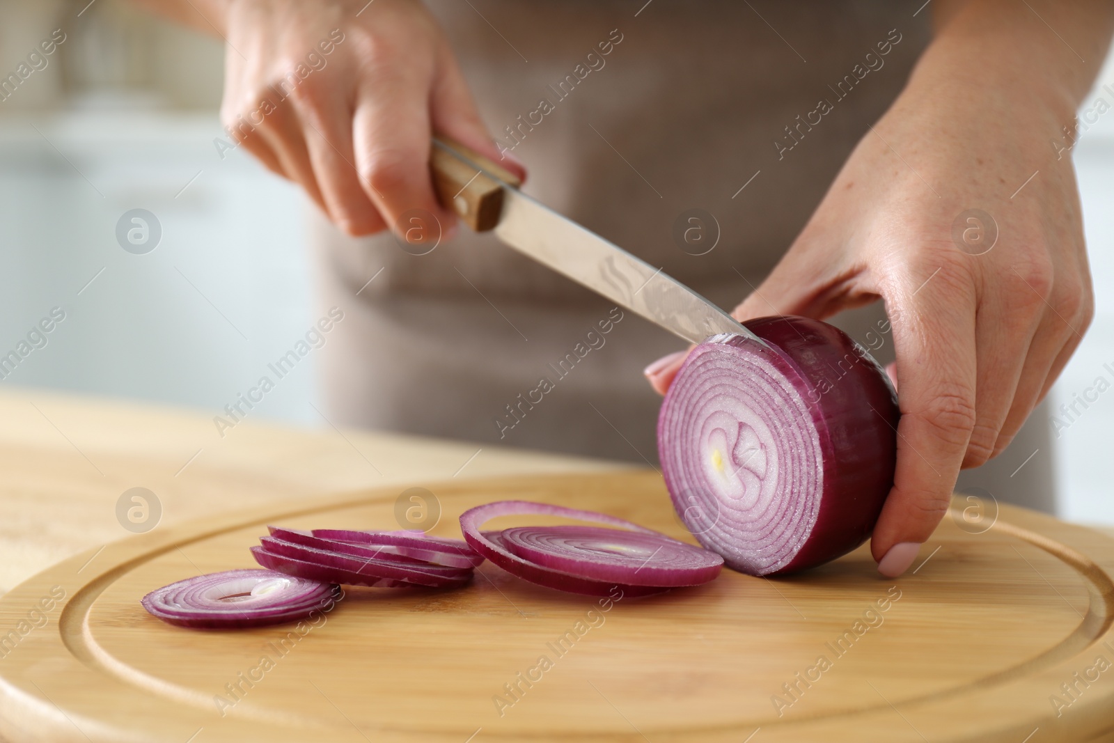 Photo of Woman cutting red onion into rings on wooden board, closeup