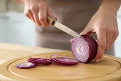Photo of Woman cutting red onion into rings on wooden board, closeup