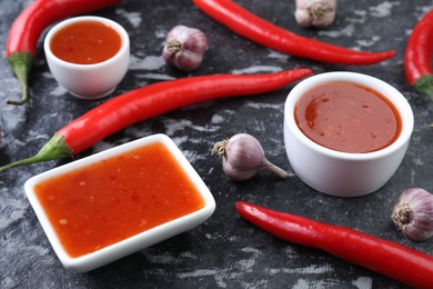 Photo of Spicy chili sauce, peppers and garlic on black textured table, closeup