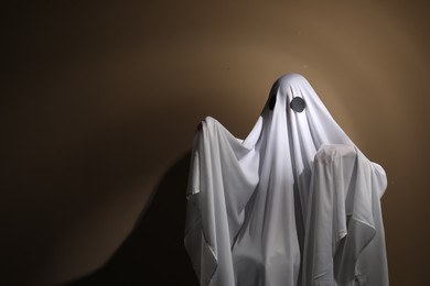 Photo of Creepy ghost. Woman covered with sheet on brown background, space for text