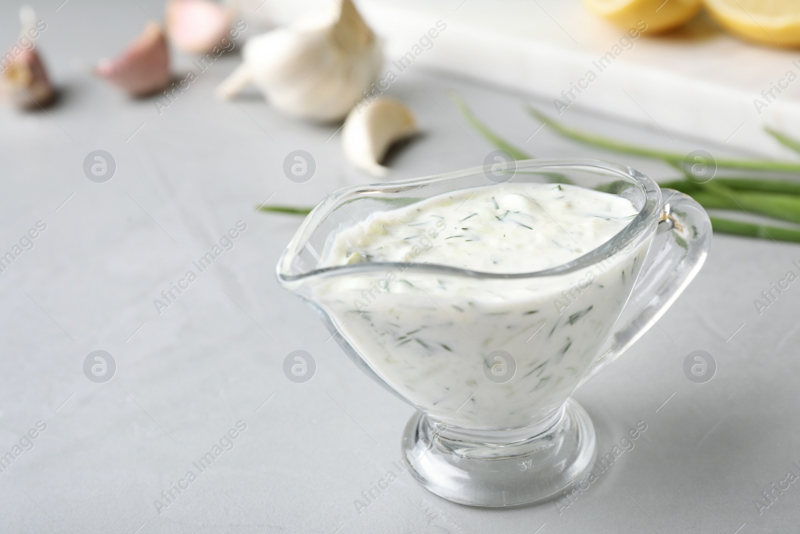 Photo of Glass gravy boat with cucumber sauce on grey table. Space for text