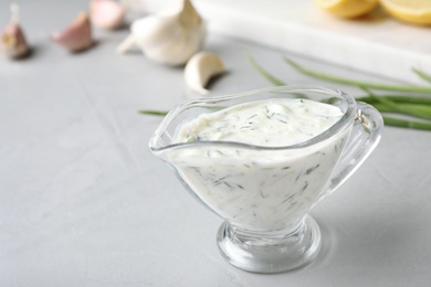 Photo of Glass gravy boat with cucumber sauce on grey table. Space for text