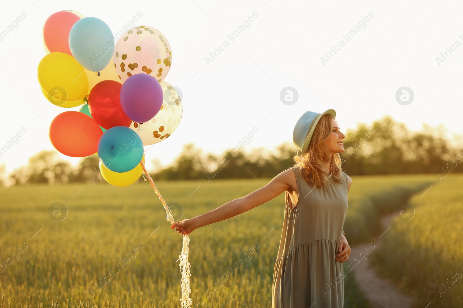 Photo of Young woman with colorful balloons in field on sunny day