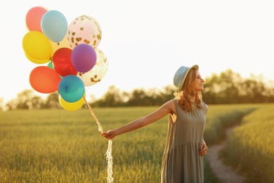 Young woman with colorful balloons in field on sunny day