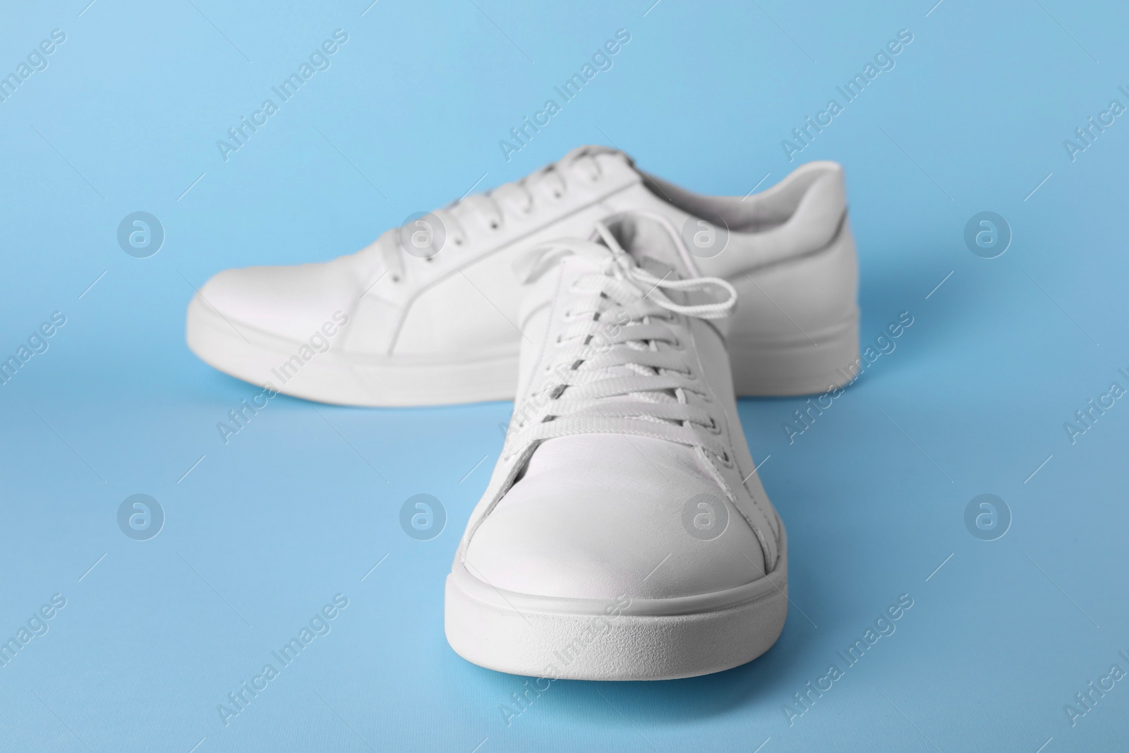 Photo of Pair of stylish white sneakers on light blue background