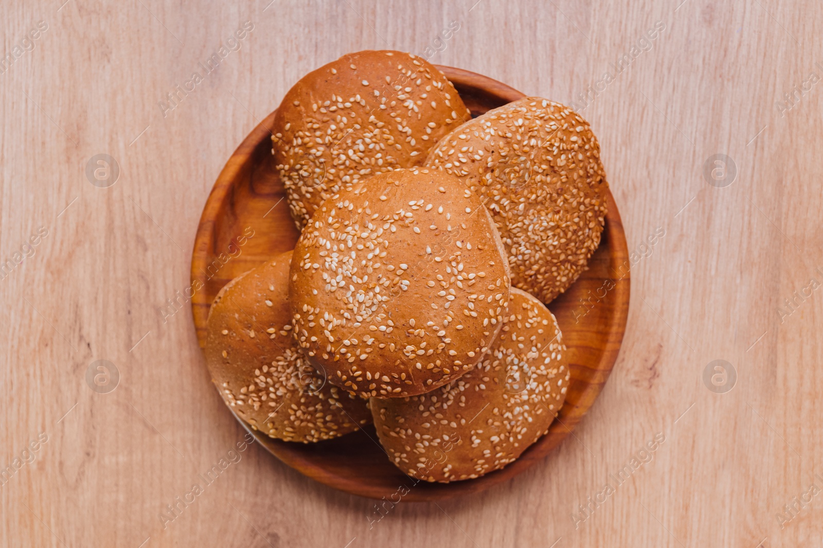 Photo of Fresh buns with sesame seeds on wooden table, top view