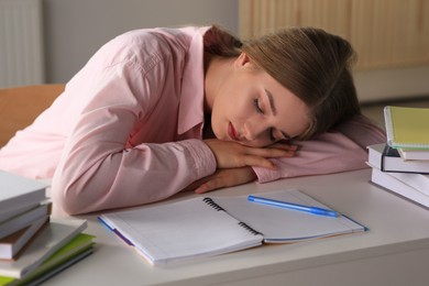 Photo of Young tired woman sleeping near books at white table indoors