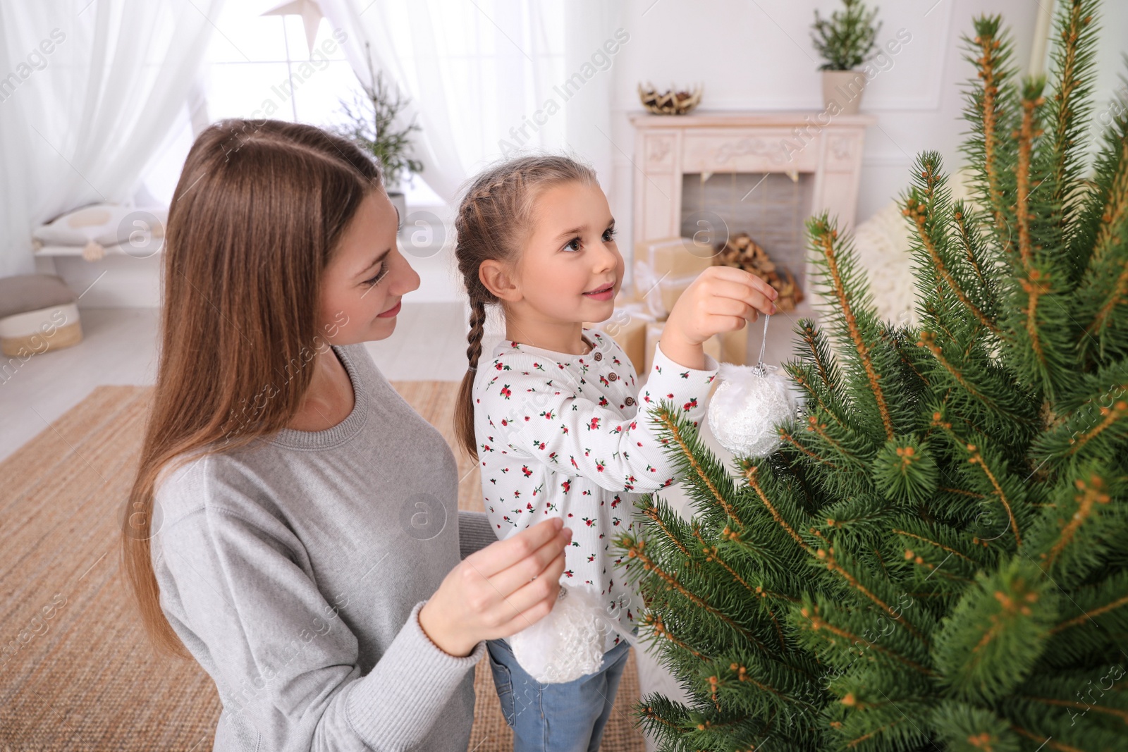 Photo of Happy mother with her cute daughter decorating Christmas tree together at home