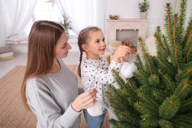 Photo of Happy mother with her cute daughter decorating Christmas tree together at home