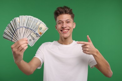 Happy man pointing at dollar banknotes on green background