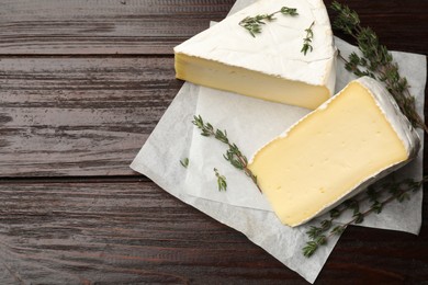 Photo of Pieces of tasty camembert cheese and thyme on wooden table, top view. Space for text