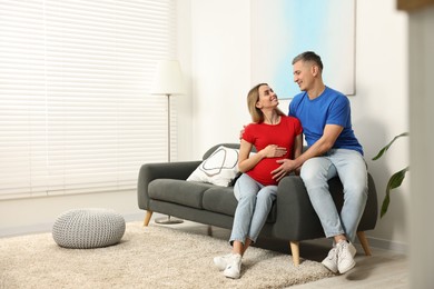 Photo of Young family housing concept. Pregnant woman with her husband on sofa at home