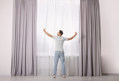 Man stretching near window with beautiful curtains at home