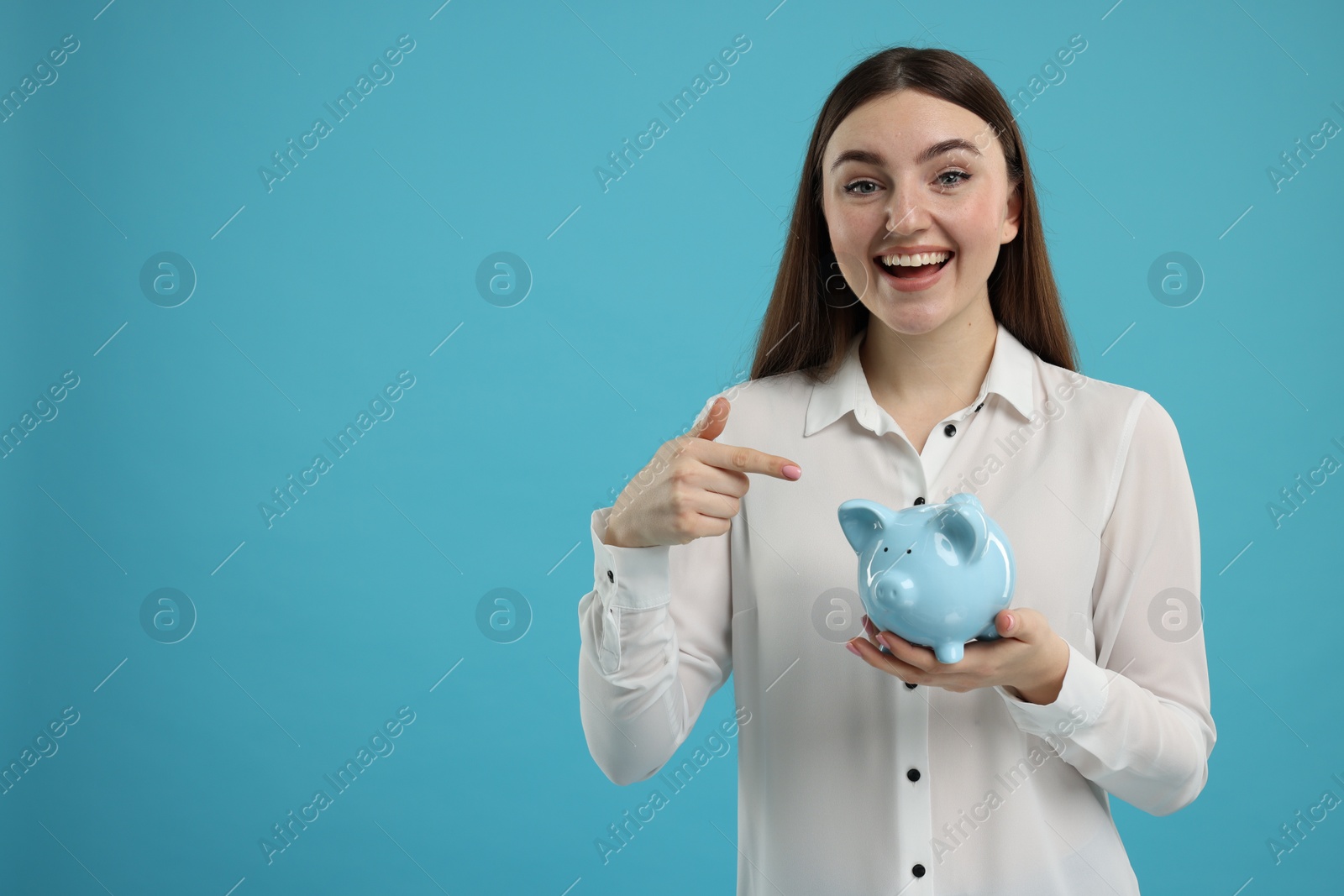 Photo of Excited woman pointing at piggy bank on light blue background, space for text