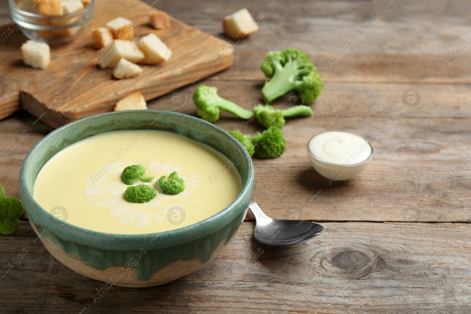 Photo of Bowl of cheese cream soup with broccoli served on wooden table, space for text